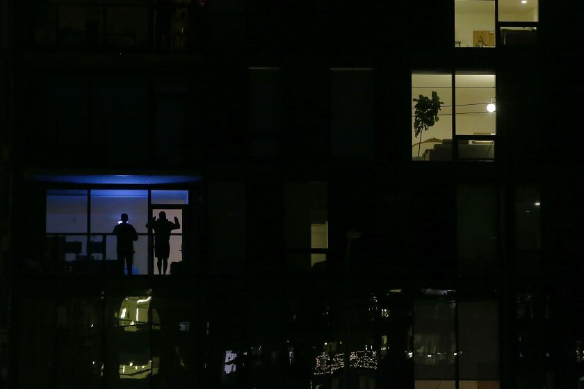Residents sheltering in place are silhouetted in a window of an apartment building in Hollywood, where a stay at home order remains in effect to help curb the spread of coronnavirus.