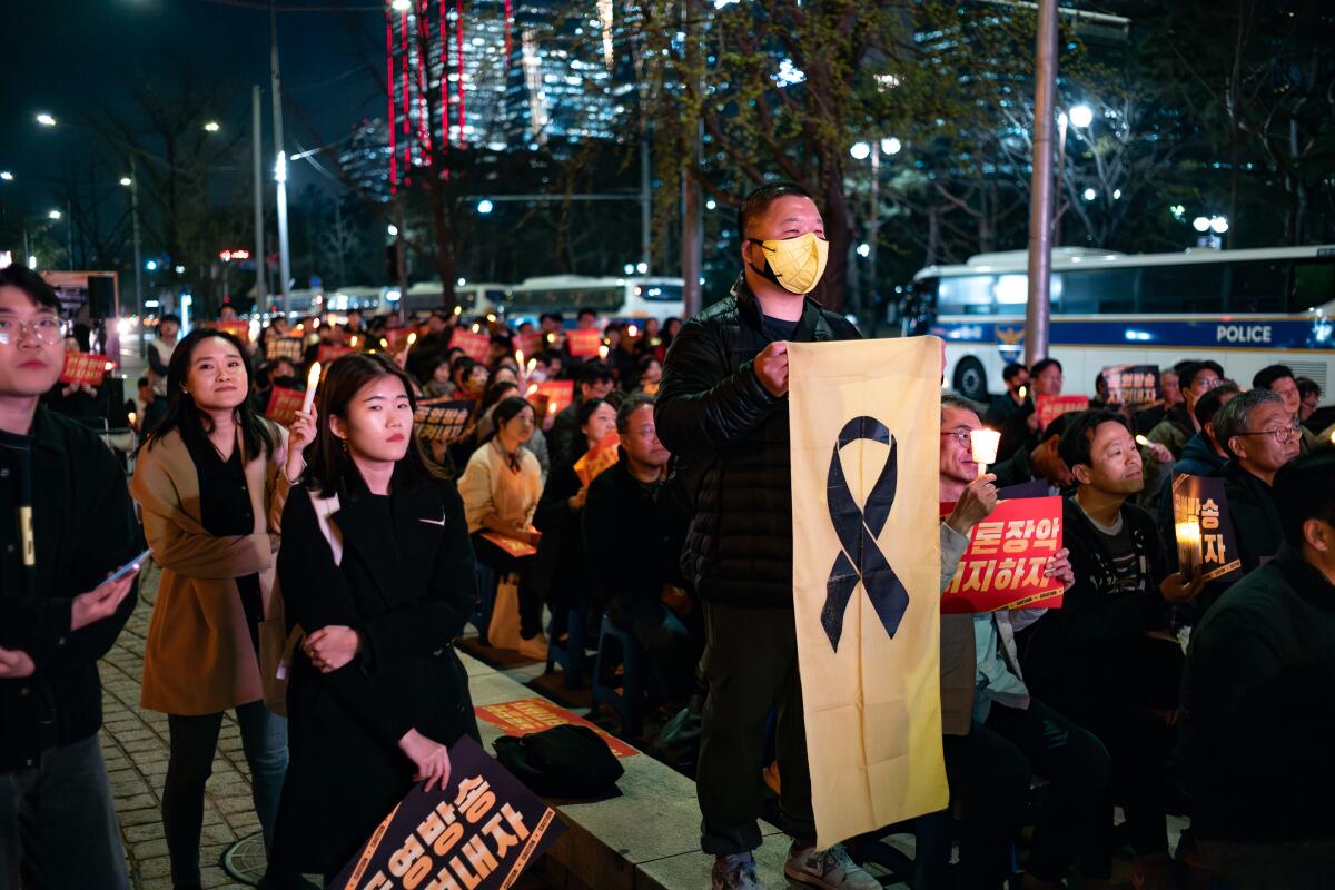 A man holding a white banner depicting a dark ribbon is surrounded by other people, some holding signs, on a street