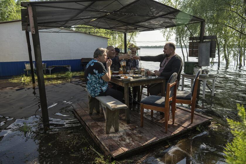 Lyudmila Kulachok, 54, left, with her family have dinner at the flooded courtyard of their house in the island of Kakhovka reservoir on Dnipro river near Lysohirka, Ukraine, Thursday, May 18, 2023. Damage that has gone unrepaired for months at a Russian-occupied dam is causing dangerously high water levels along a reservoir in southern Ukraine. (AP Photo/Evgeniy Maloletka)