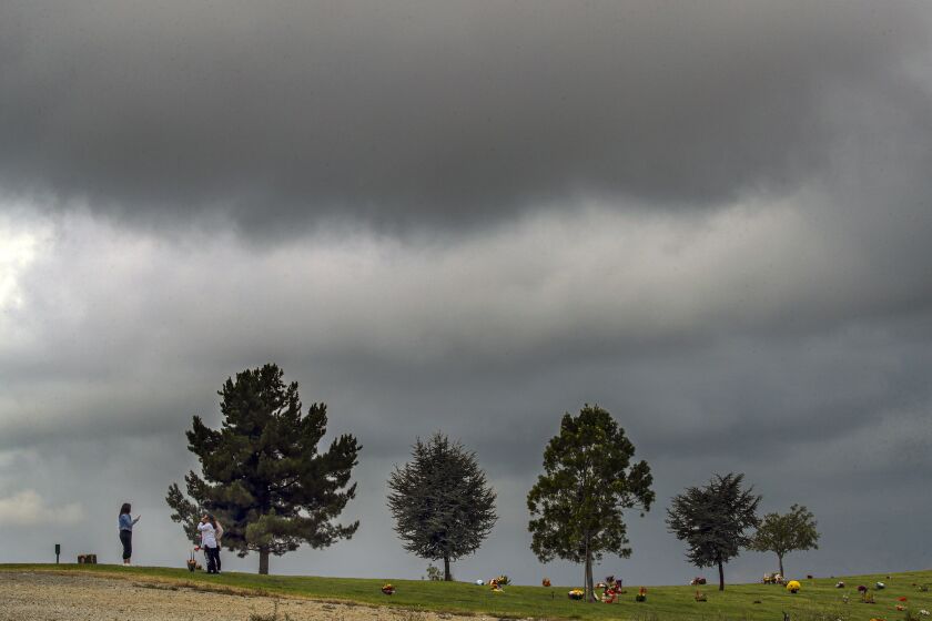 Los Angeles, CA - October 23: A family visits loved one at Forest Lawn Cemetery on a cloudy Saturday morning, Oct. 23, 2021 in Covina, CA. (Irfan Khan / Los Angeles Times)