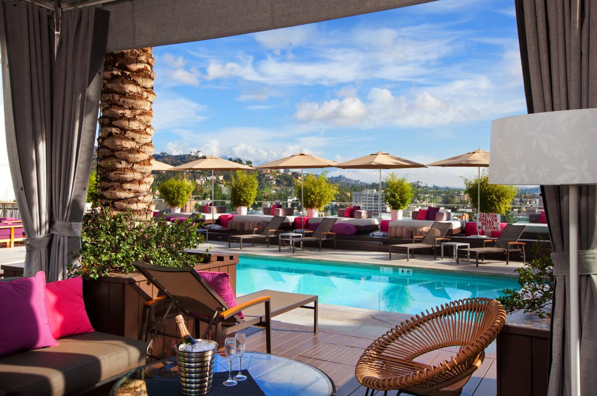 A pool is seen from inside a cabana with a low table and champagne chilling in a bucket.