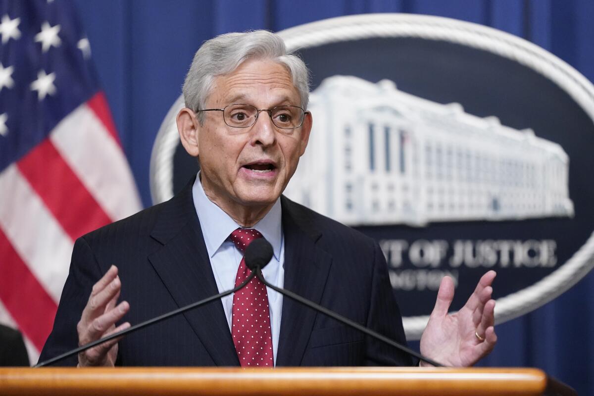 A man speaking into microphones in front of the Department of Justice logo and an American flag 