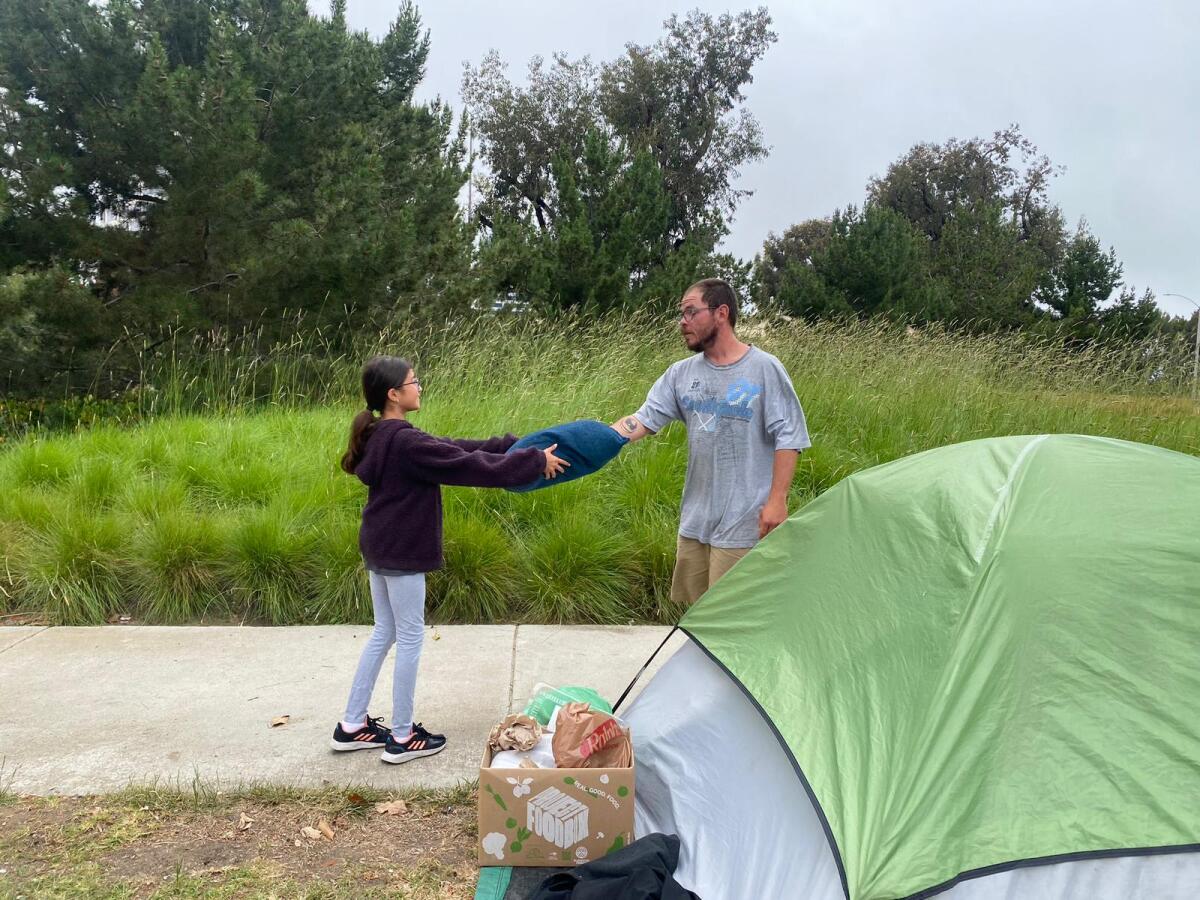 Arianna Akbari hands a pillow to a homeless man near the Fashion Island bus stop.