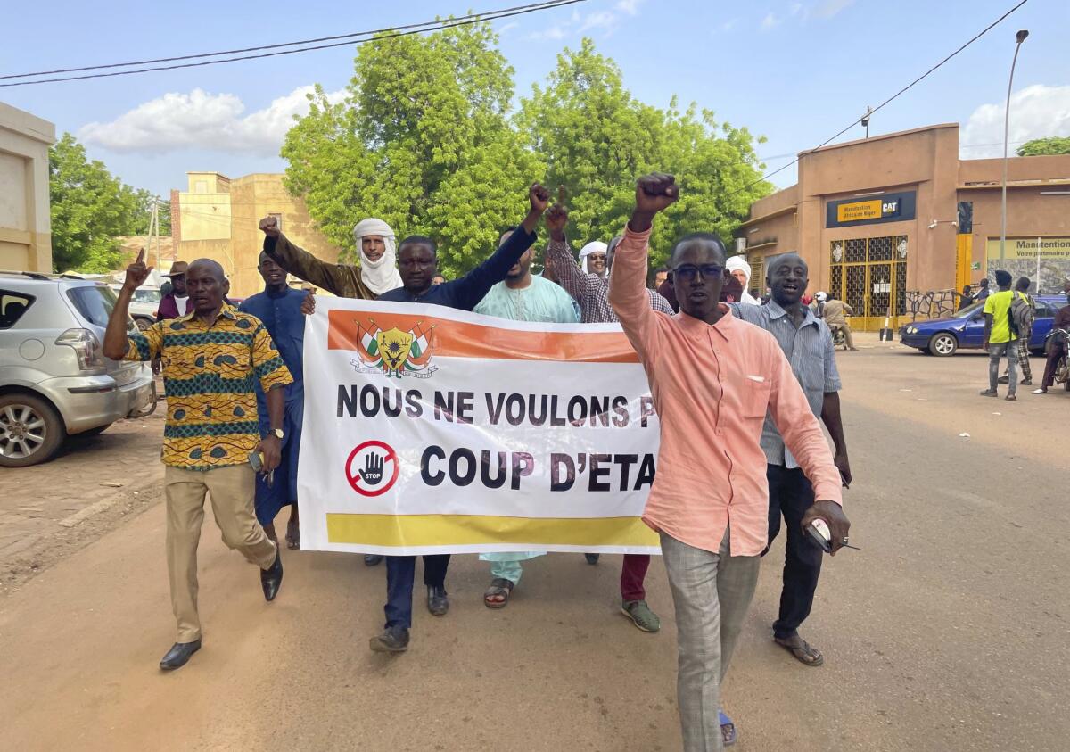 People walk down a street in Niger with a banner reading in French "We do not want a coup d'etat."