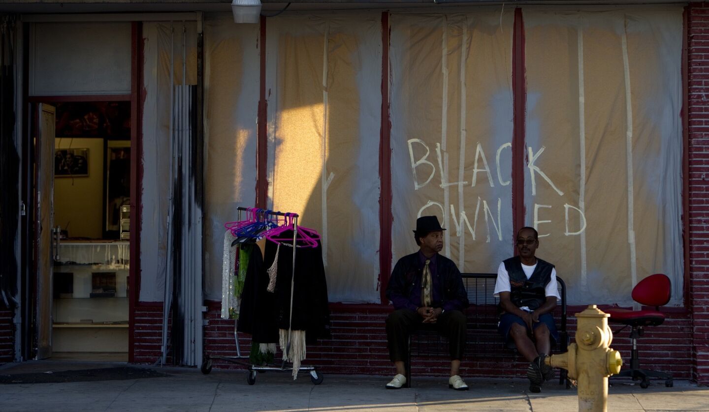 Business owners sit outside a beauty supply shop with the words "black owned" written on the windows. Tuesday marked the third day of protests on Crenshaw Boulevard near Leimert Park.