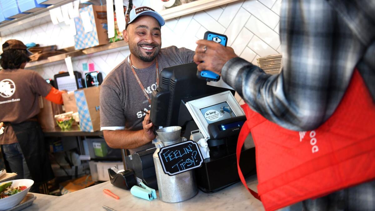 A worker at Mendocino Farms in El Segundo checks on an order being picked up by a DoorDash delivery worker.