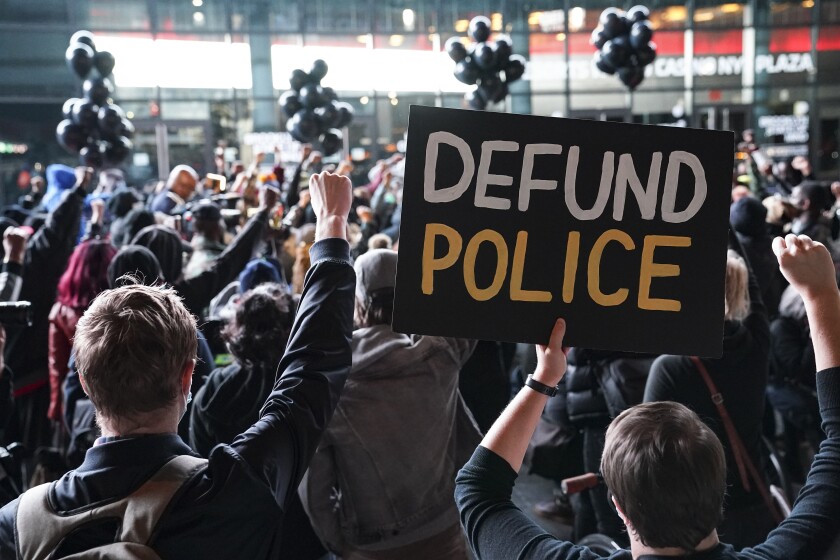A protester stands in a crowd and holds a sign that reads "Defund Police" 