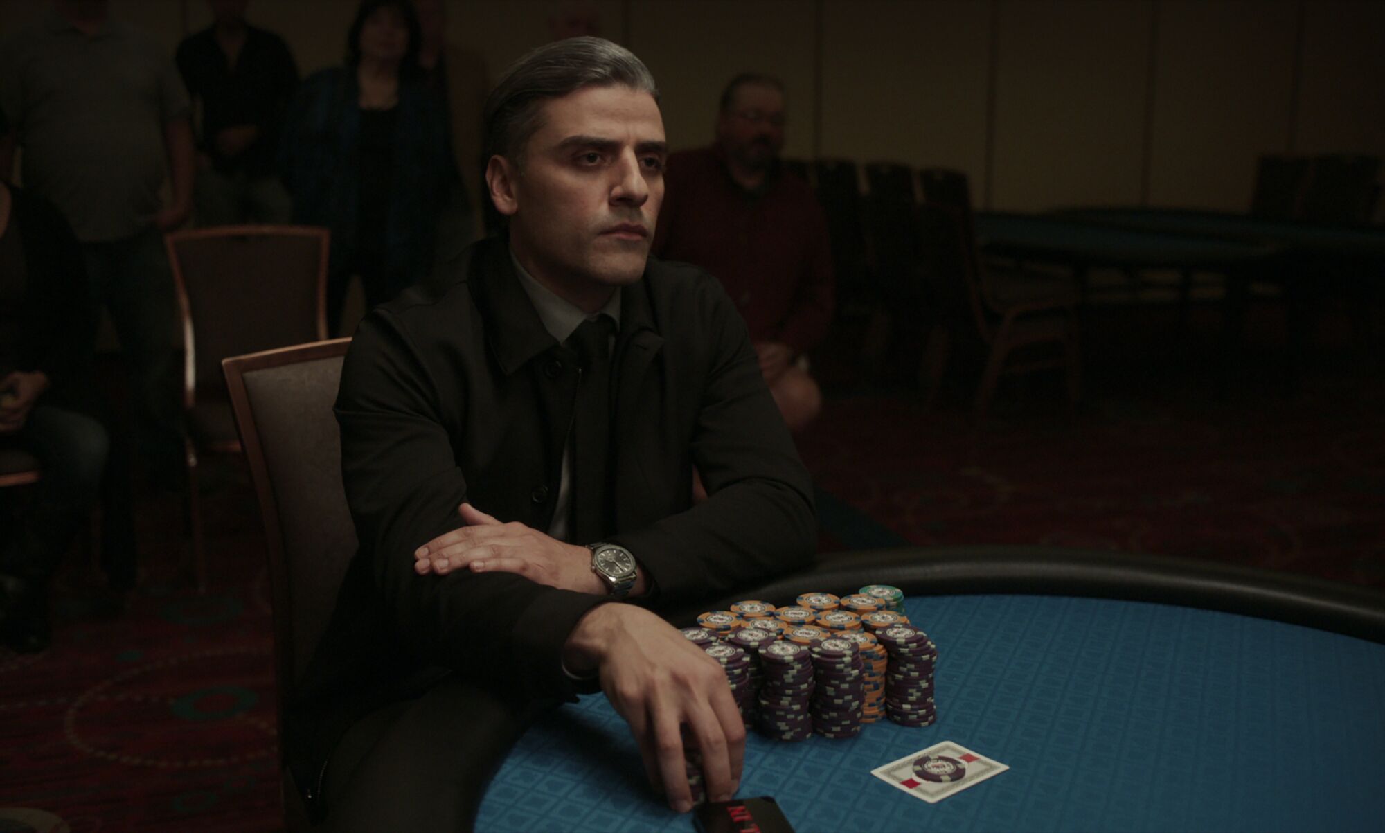Oscar Isaac sits at a card table with stacks of chips in front of him.