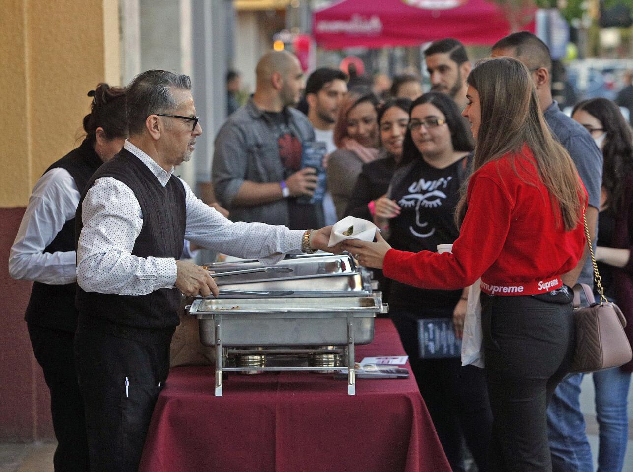 El Morfi Grill owner Rene Vildoza hands an empanada sample to a woman at the start of a very long line at Taste Walk Glendale on Wednesday, May 1, 2019. About sixty-five restaurants and local vendors set up to give those with wristbands free samples.