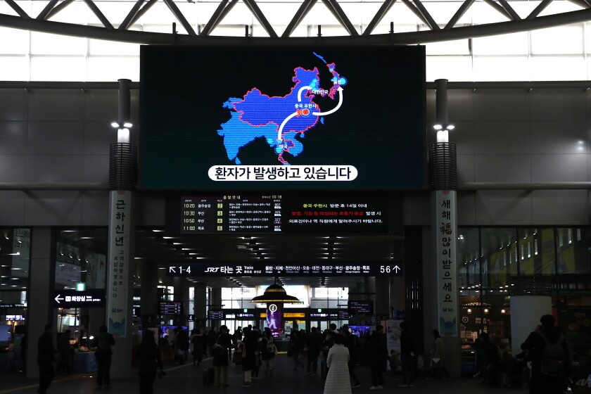 Passengers walk under a monitor displaying information on the Wuhan coronavirus at SRT train terminal on Thursday in Seoul. So far, two cases of the virus have been confirmed in South Korea.