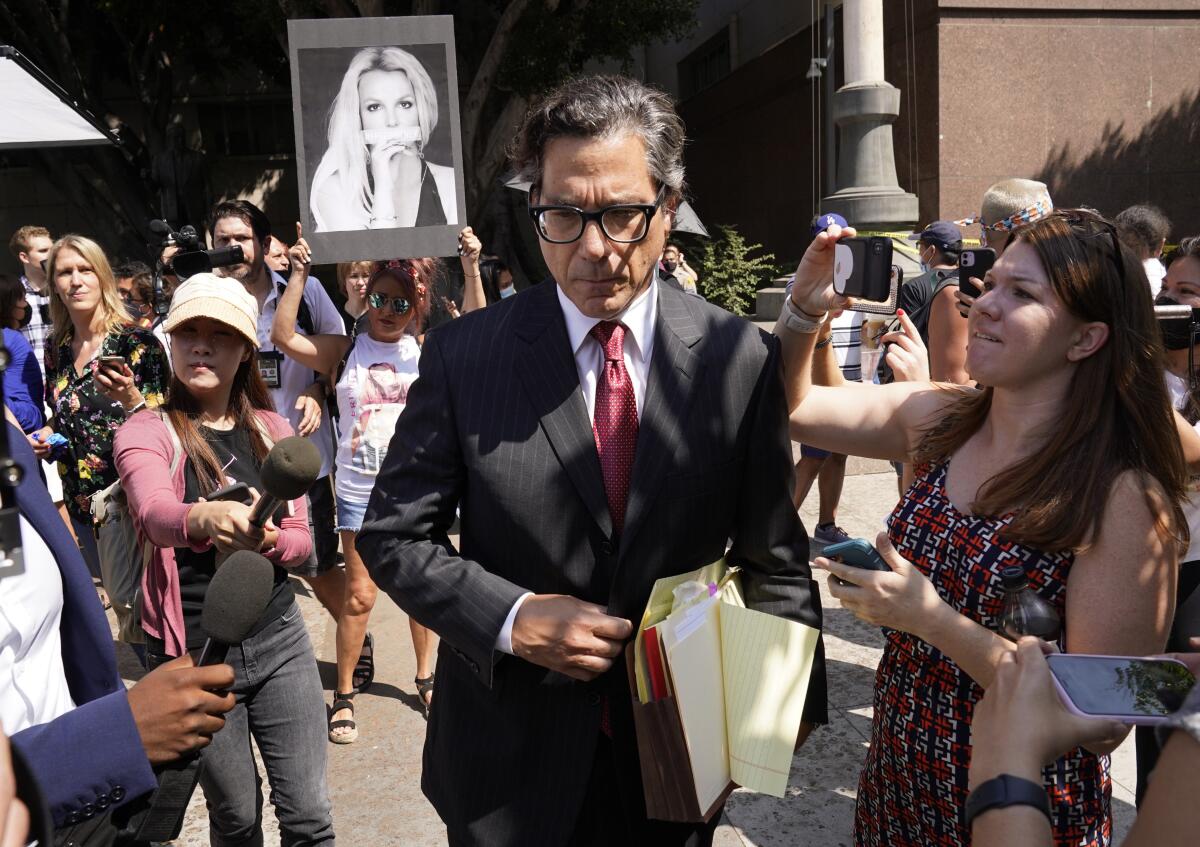 A man in a suit is surrounded by people with microphones and cameras