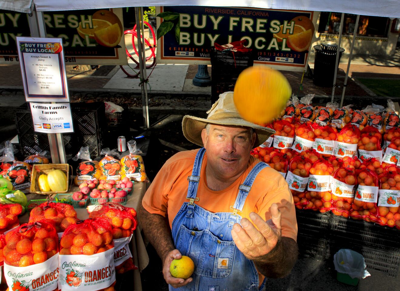 Brian Griffith, owner of the Griffith Family Farms, tosses one of his Valencia oranges into the air in his booth at the Claremont Farmers & Artisans Market in the Claremont Village.