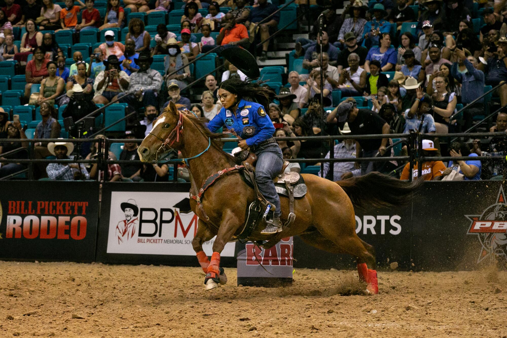A woman and her horse race by a barrel at a rodeo as a crowd watches from the stands