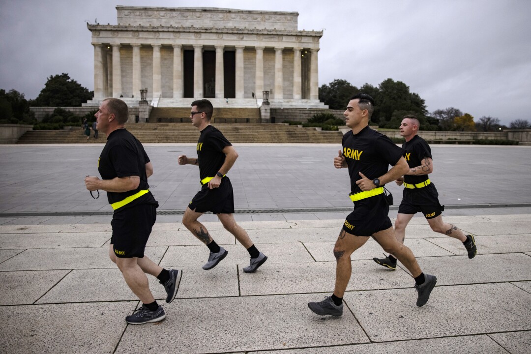 Four soldiers in black T-shirts and shorts labeled "Army" run past the Lincoln Memorial.