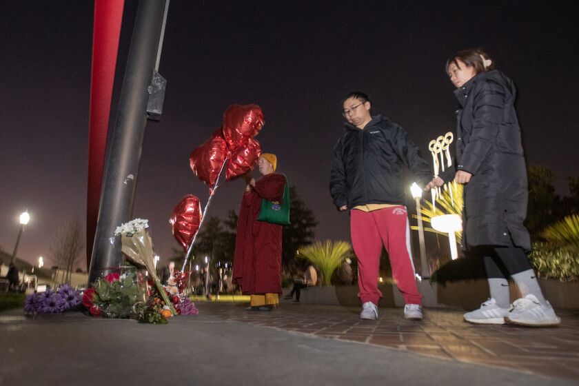 Monterey Park, CA - January 22: People who brought flowers join another paying their respects at a memorial for Monterey Park mass shooting victims after a news conference at the Monterey Park Civic Center Sunday, Jan. 22, 2023. (Allen J. Schaben / Los Angeles Times)