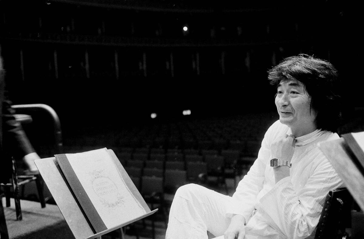 Conductor Seiji Ozawa leans back in a chair and smiles in a black-and-white photo from 1982.