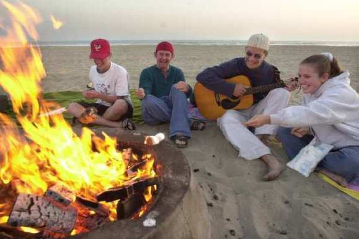 A group of friends gather by a fire ring in Newport Beach. Air regulators are considering a ban on the Southern California tradition.