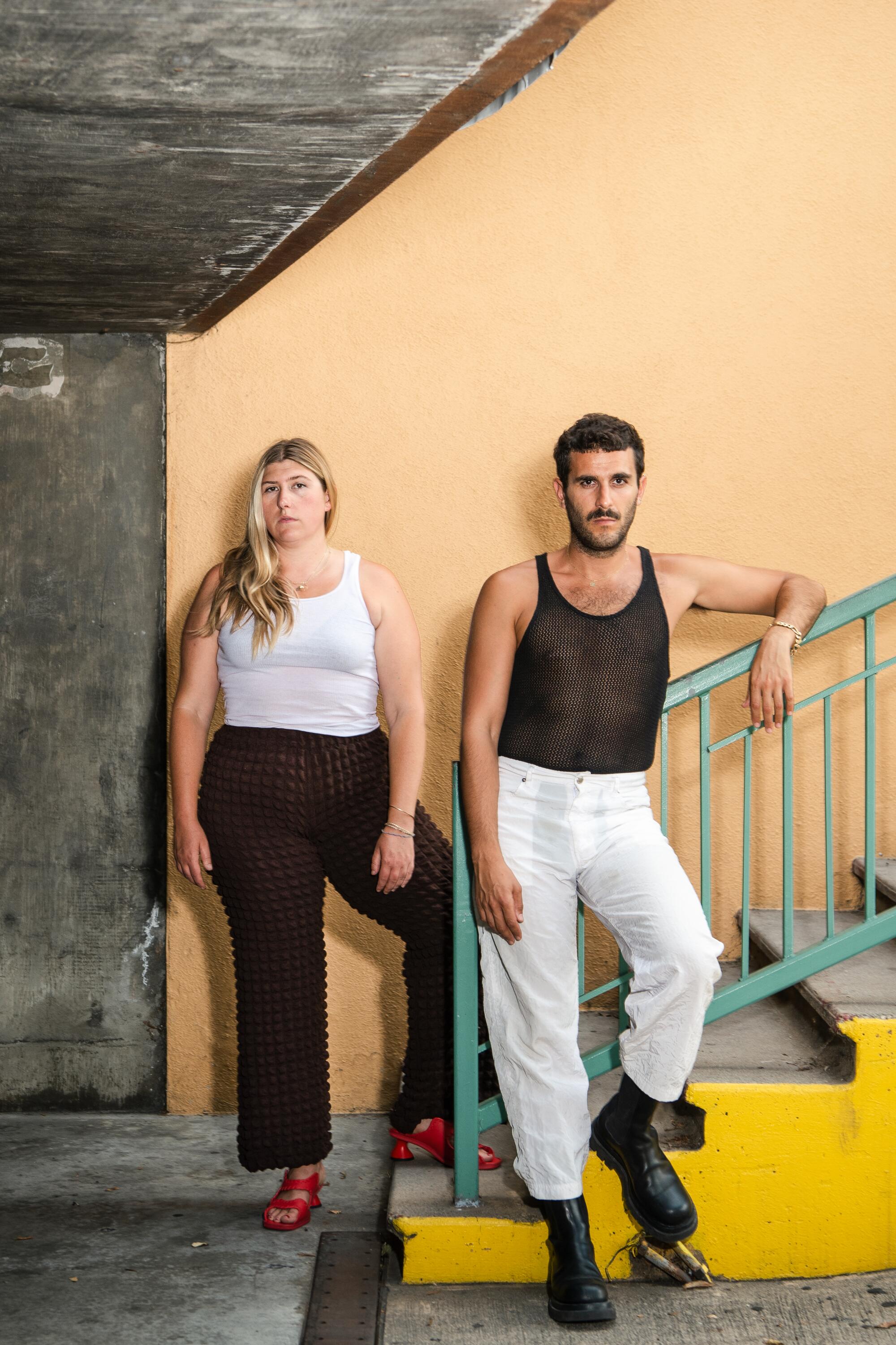 A woman and man pose beside a staircase with a green railing.