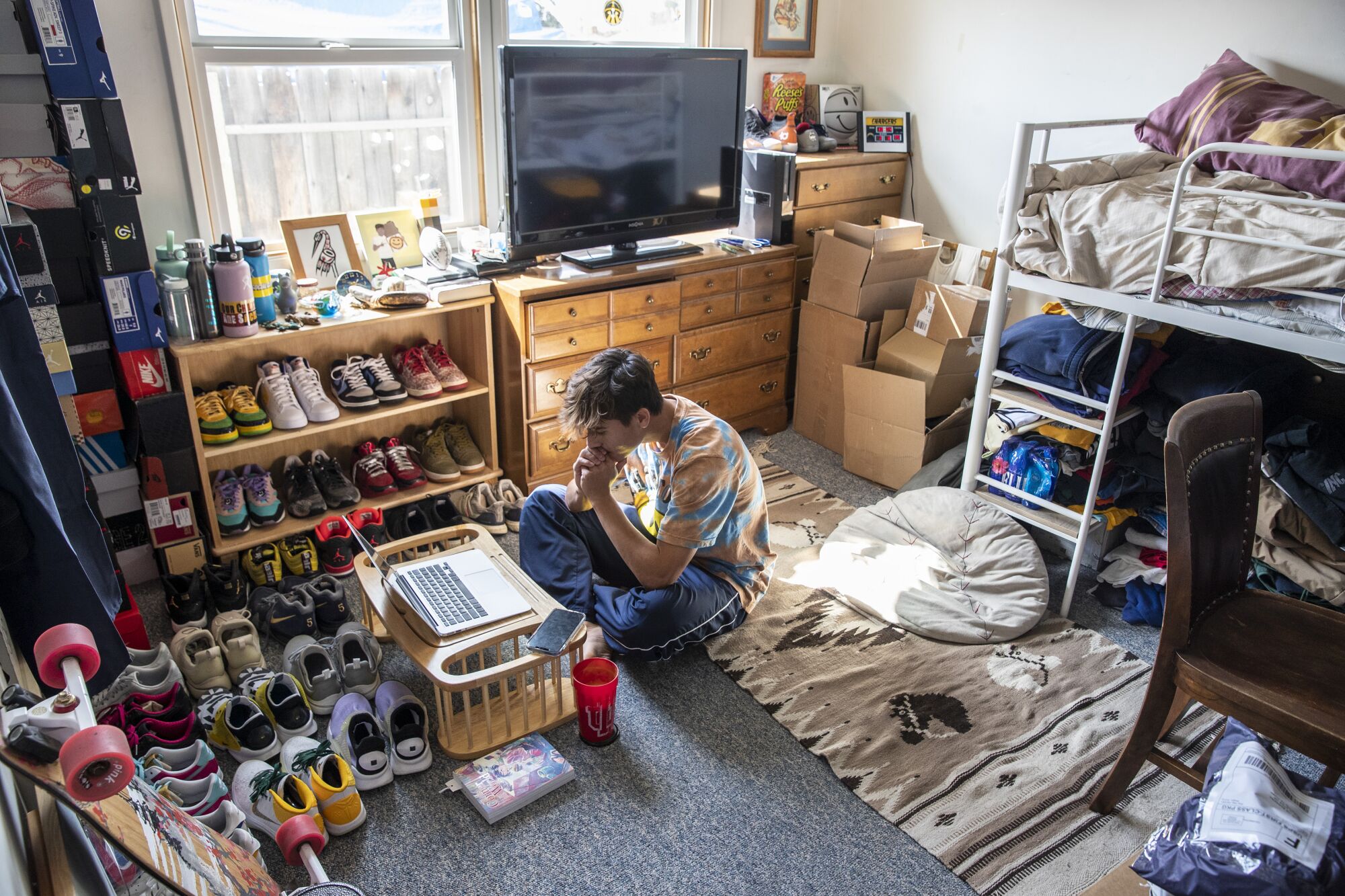 A student sits on the floor of his bedroom watching an online class. 