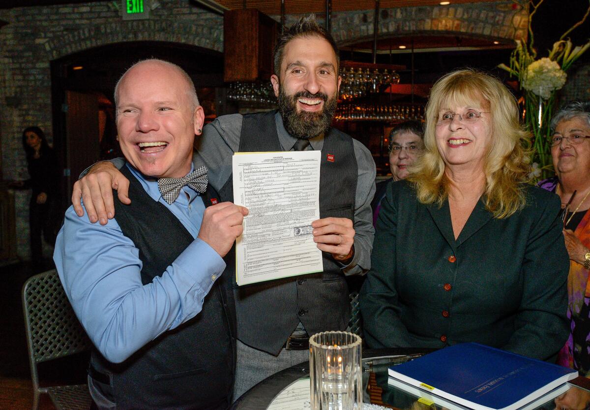 Aubrey Loots, left, and Danny Leclair, standing next to notary public Marilyn Townsend, display their signed marriage certificate just days before their Rose Parade wedding. Loots and Leclair will wed on the AIDS Healthcare Foundation's float on New Year's Day.