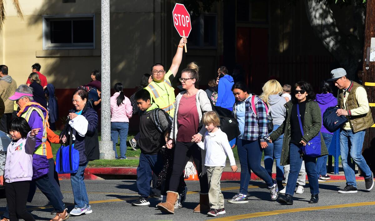 A crossing guard holds up a stop sign as parents walk schoolchildren across a street.