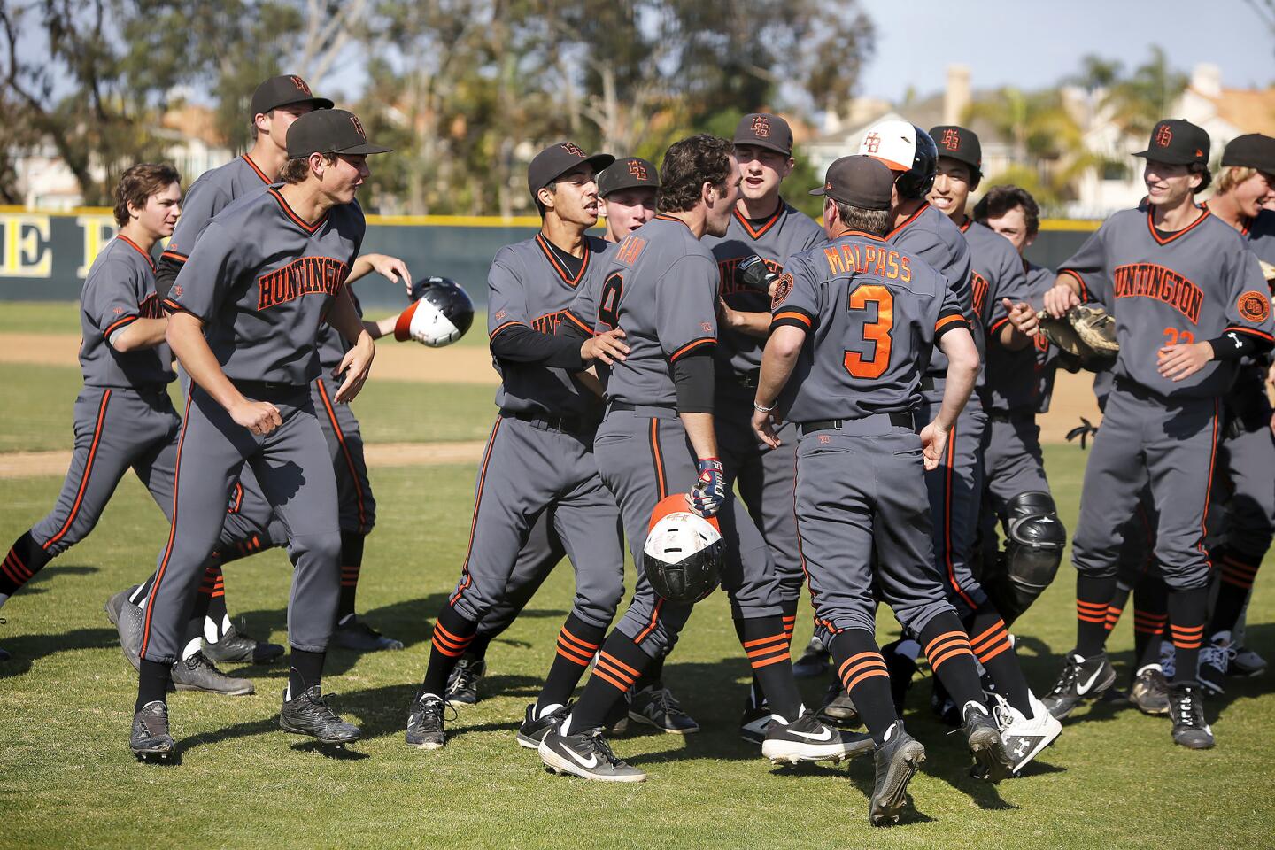 Huntington Beach High players swarm out of the dugout to celebrate with Josh Hahn (9) after he hit a second-inning grand slam to go ahead in the Surf League game at Edison on Friday.