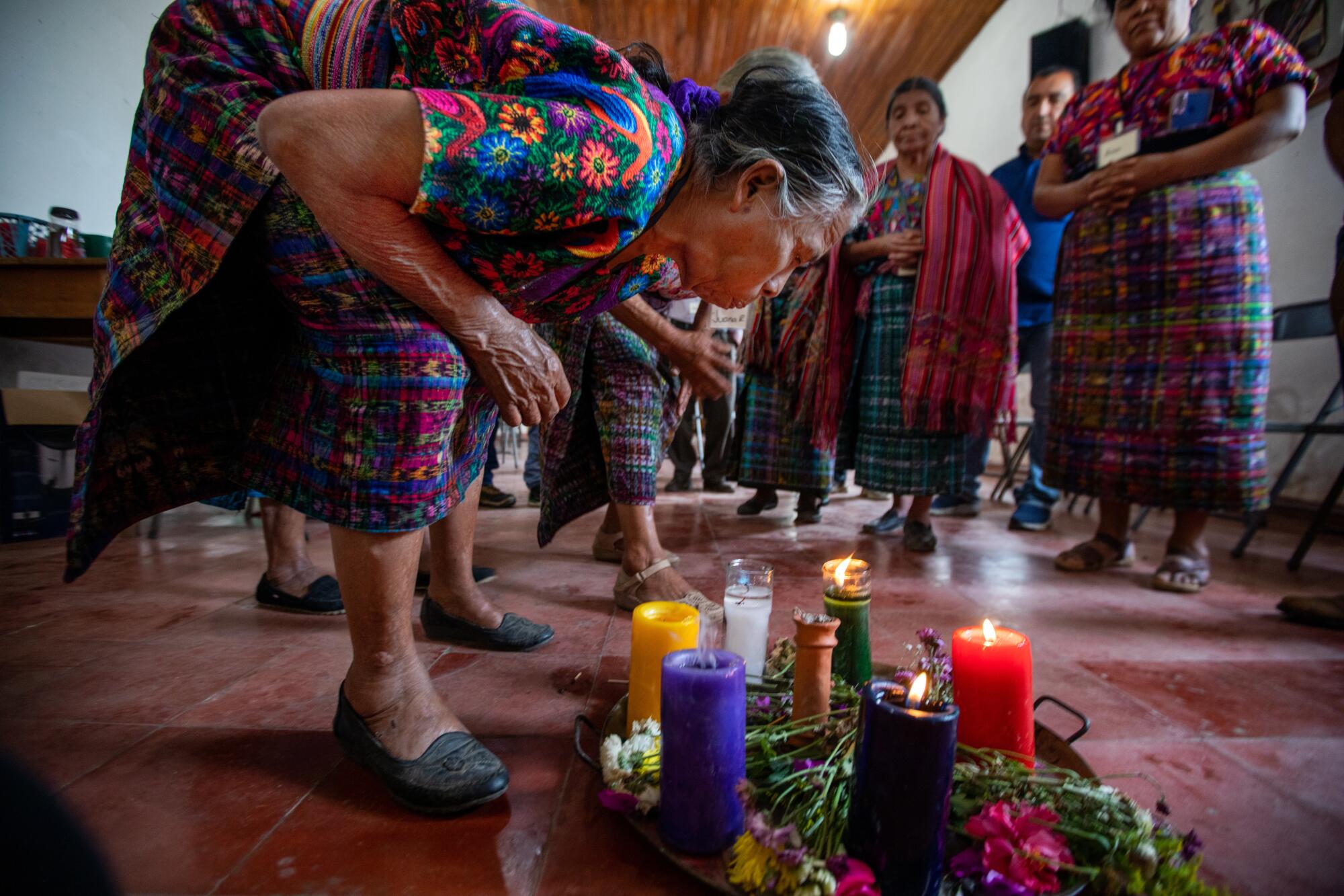 A woman in colorful dress blows out one of the candles at her feet 