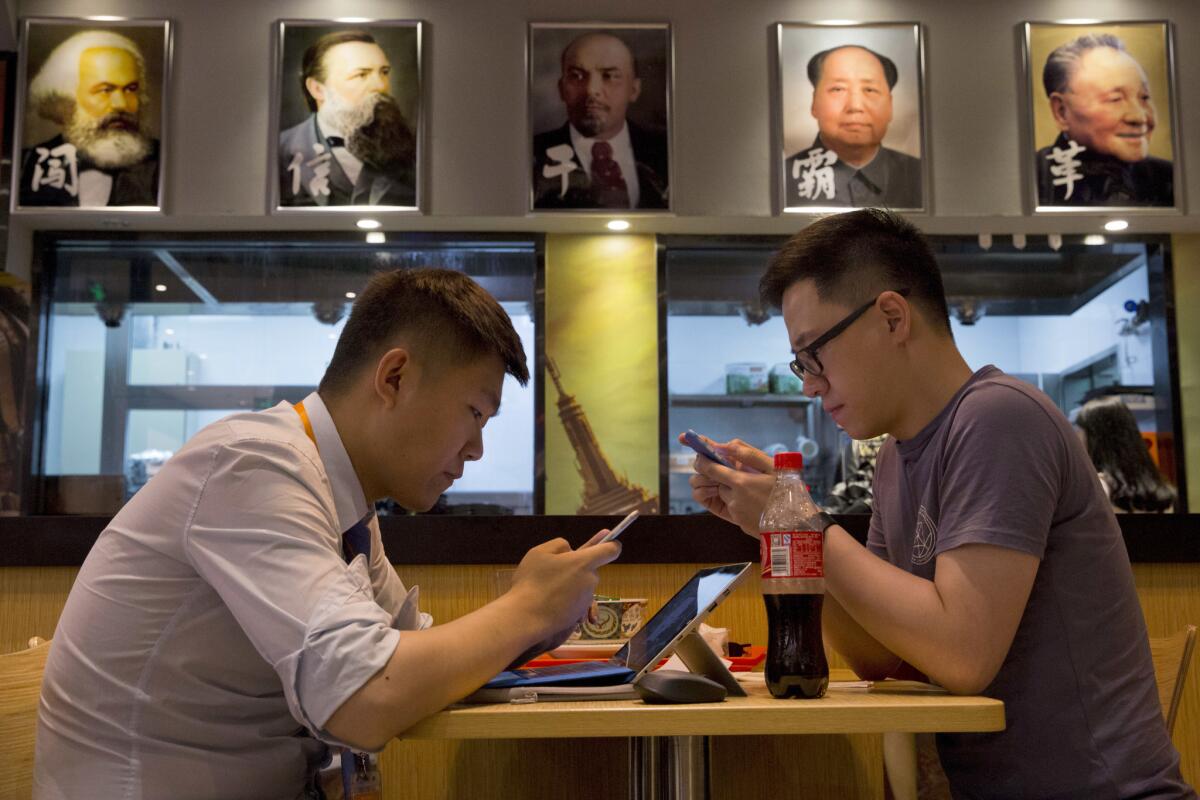 Customers look at their mobile devices in a noodle restaurant displaying portraits of former Communist leaders including, from left, Karl Marx, Friedrich Engels, Vladimir Lenin, Mao Zedong and Deng Xiaoping in Beijing on July 3, 2016.