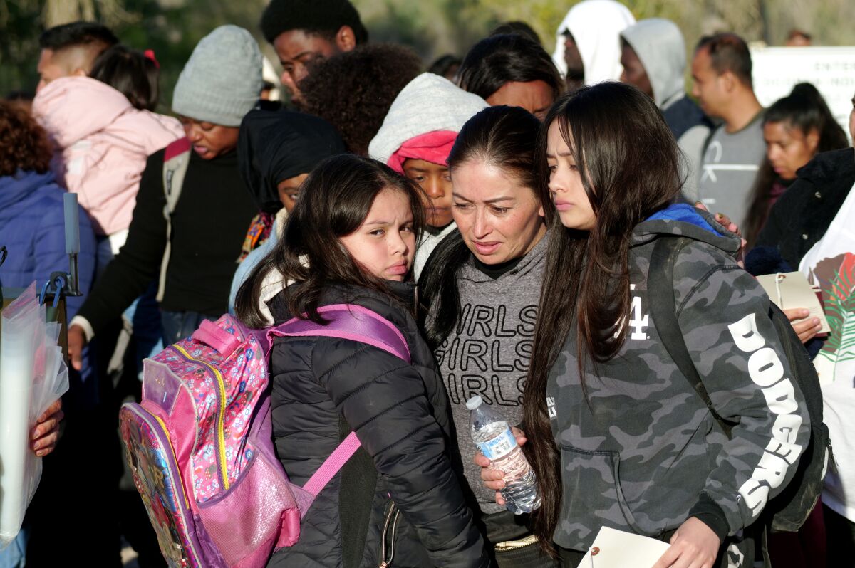 A girl wearing a backpack huddles with a woman and another girl in the sun as others stand nearby