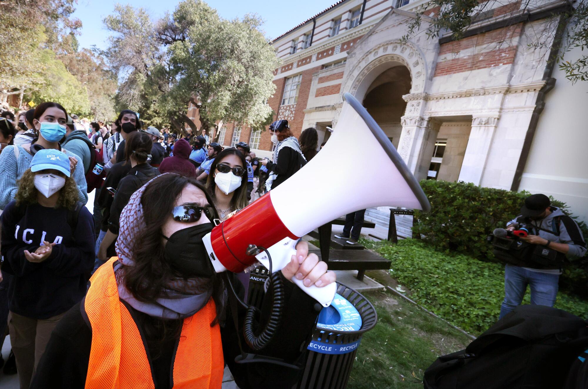 A person uses a bullhorn on UCLA campus among several other people, all in masks.