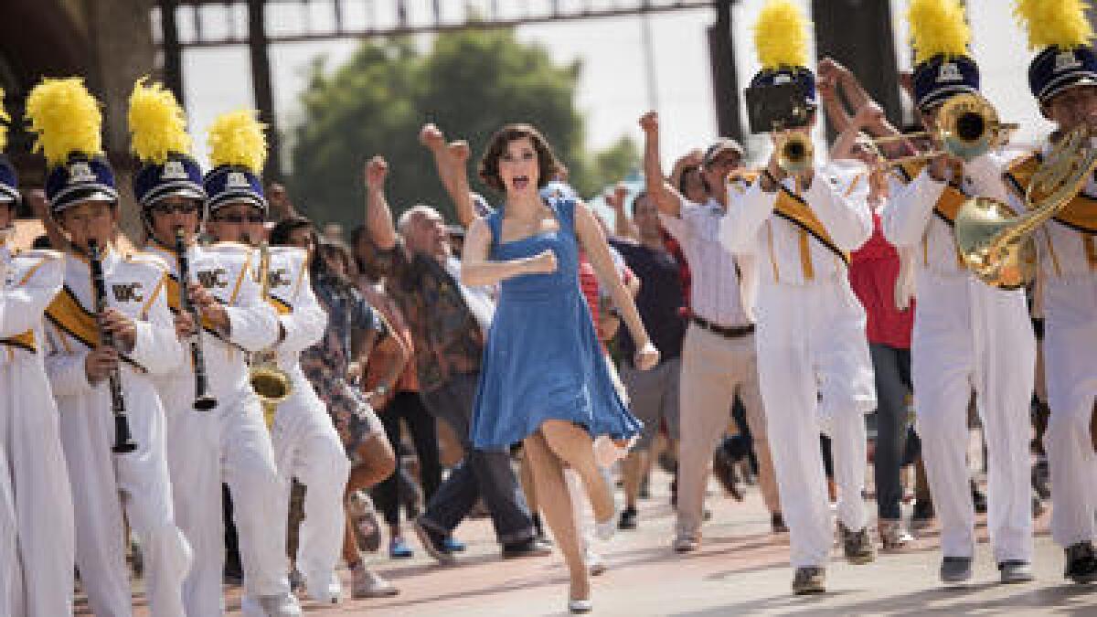 A woman in a blue dress marches with a marching band.