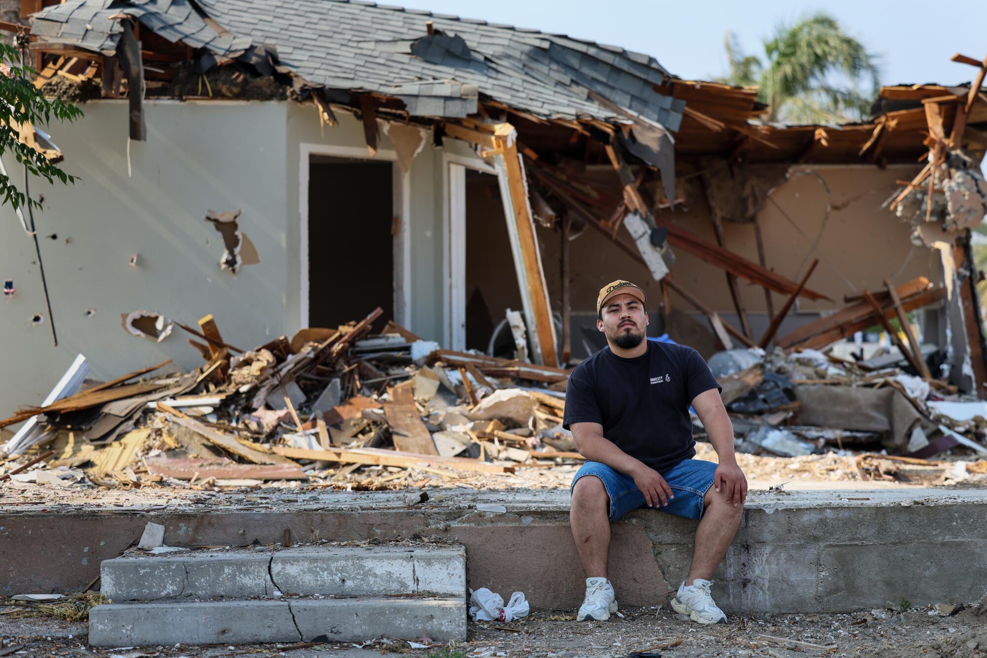 A man sits in front of a home undergoing demolition. 