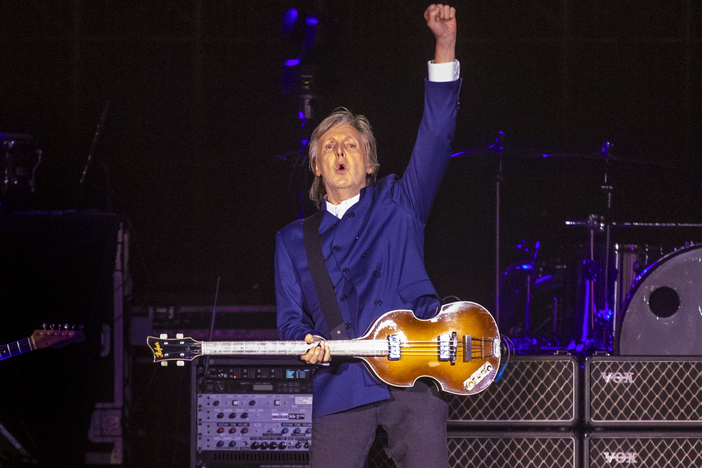Paul McCartney, with bass, thrusts a fist in the air in concert