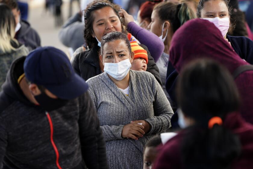 A woman waits for food handouts from a local church at a makeshift camp for migrants seeking asylum in the United States at the border crossing Friday, March 12, 2021, in Tijuana, Mexico. The Biden administration hopes to relieve the strain of thousands of unaccompanied children coming to the southern border by terminating a 2018 Trump-era order that discouraged potential family sponsors from coming forward to house the children. (AP Photo/Gregory Bull)