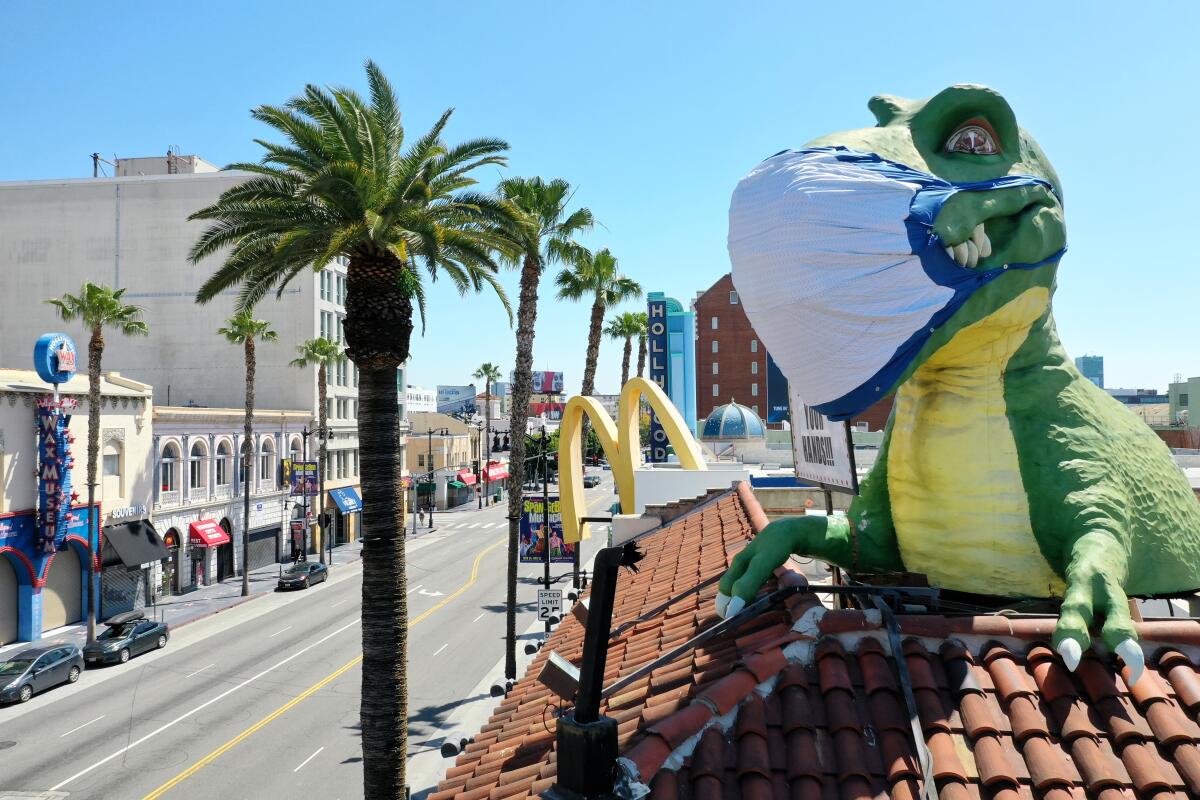 A giant T-Rex wearing a protective mask sends a coronavirus message to a mostly empty intersection of Hollywood Blvd. and Highland Ave. from the top of Ripley's Believe It or Not! Odditorium, which is temporarily closed.