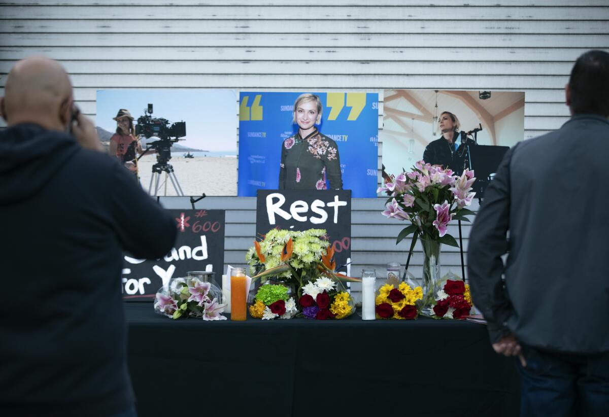 A table covered with flower arrangements before photos on a wall of a young woman.