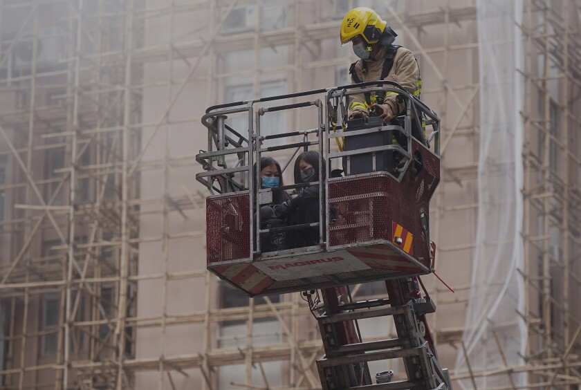 Two women are rescued by a firefighter in a bucket crane outside the World Trade Centre located in the city's popular Causeway Bay shopping district of Hong Kong, Wednesday, Dec. 15, 2021. Dozens of people were trapped on the rooftop of the Hong Kong skyscraper after a major fire broke out Wednesday, as firefighters rushed to rescue them and put out the blaze. (AP Photo)