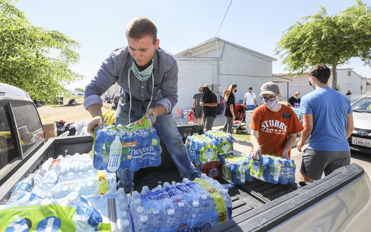 Volunteers load cases of plastic water bottles into the back of a pickup truck at school district offices