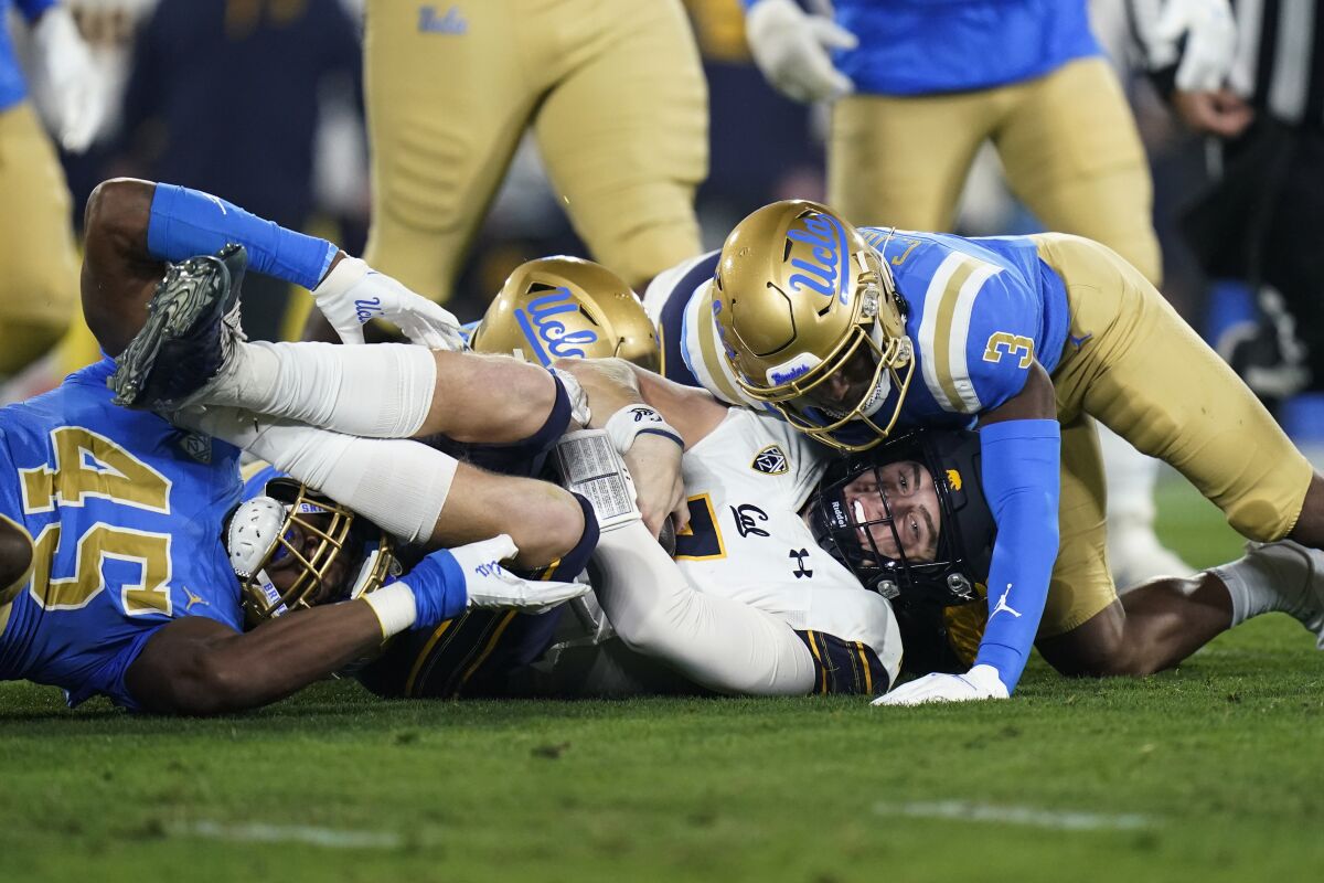 Cal quarterback Chase Garbers is brought down by UCLA defensive back Cameron Johnson, right, and linebacker Mitchell Agude.
