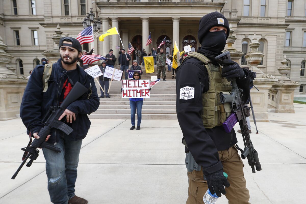 FILE - In this April 15, 2020 file photo, protesters carry rifles near the steps of the Michigan State Capitol building in Lansing, Mich. A plot to kidnap Michigan’s governor has put a focus on the security of governors who have faced protests and threats over their handling of the coronavirus pandemic. The threats have come from people who oppose business closures and restrictions on social gatherings. (AP Photo/Paul Sancya File)