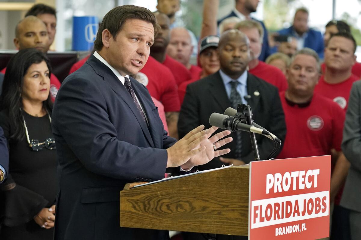 Florida Gov. Ron DeSantis stands behind a lectern, which has a "Protect Florida jobs" sign on it.