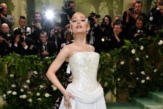 Ariana Grande poses in a white gown and tilts her chin up while walking a green carpet