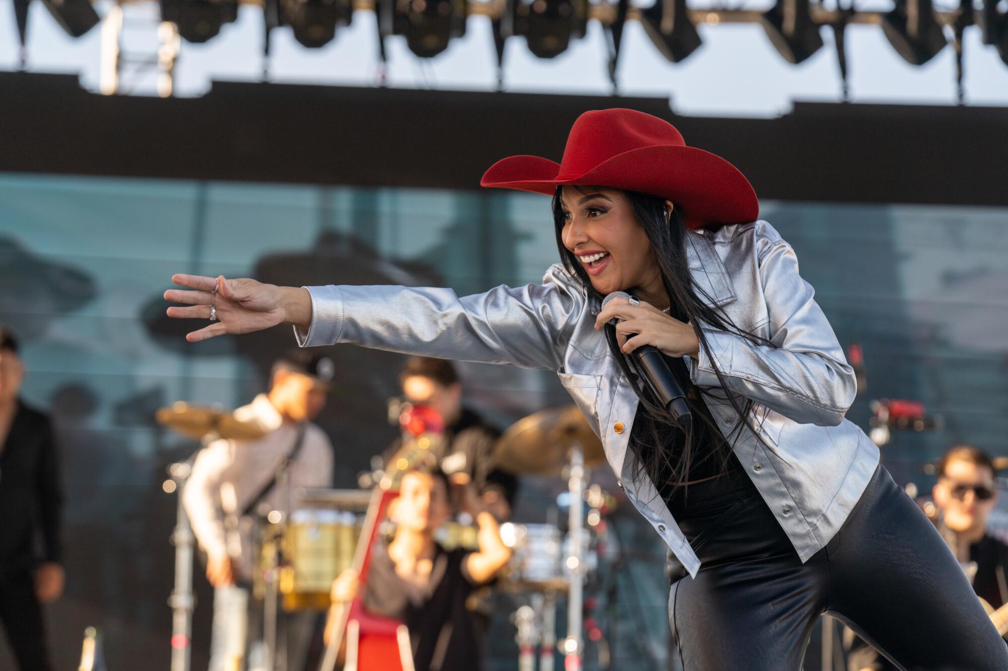 A woman holding a mic near her face reaches toward the audience from a stage. 