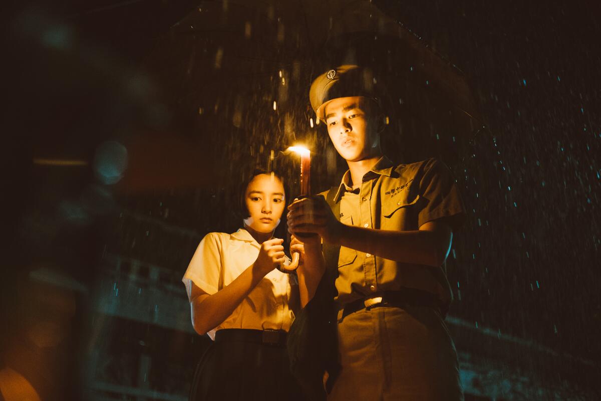 A female and a male high school student under an umbrella with a candle.