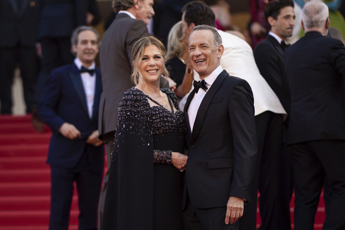 Rita Wilson and Tom Hanks smile and pose together in black formal attire on a red carpet in Cannes