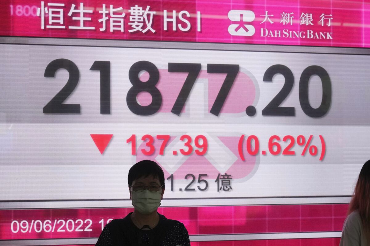 A woman wearing a face mask stands in front of a bank's electronic board showing the Hong Kong share index in Hong Kong, Thursday, June 9, 2022. Shares were mostly lower in Asia on Thursday as investors watched for fresh signs of inflation and crude oil prices hovered above $120 a barrel, adding to price pressures. (AP Photo/Kin Cheung)