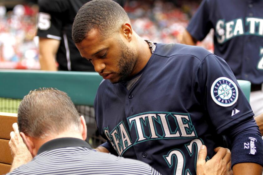 Mariners second baseman Robinson Cano (22) is led from the dugout by trainer Rob Nodine after getting hit in the forehead with an errant throw by an Angels player during warmups in the seventh inning Saturday.
