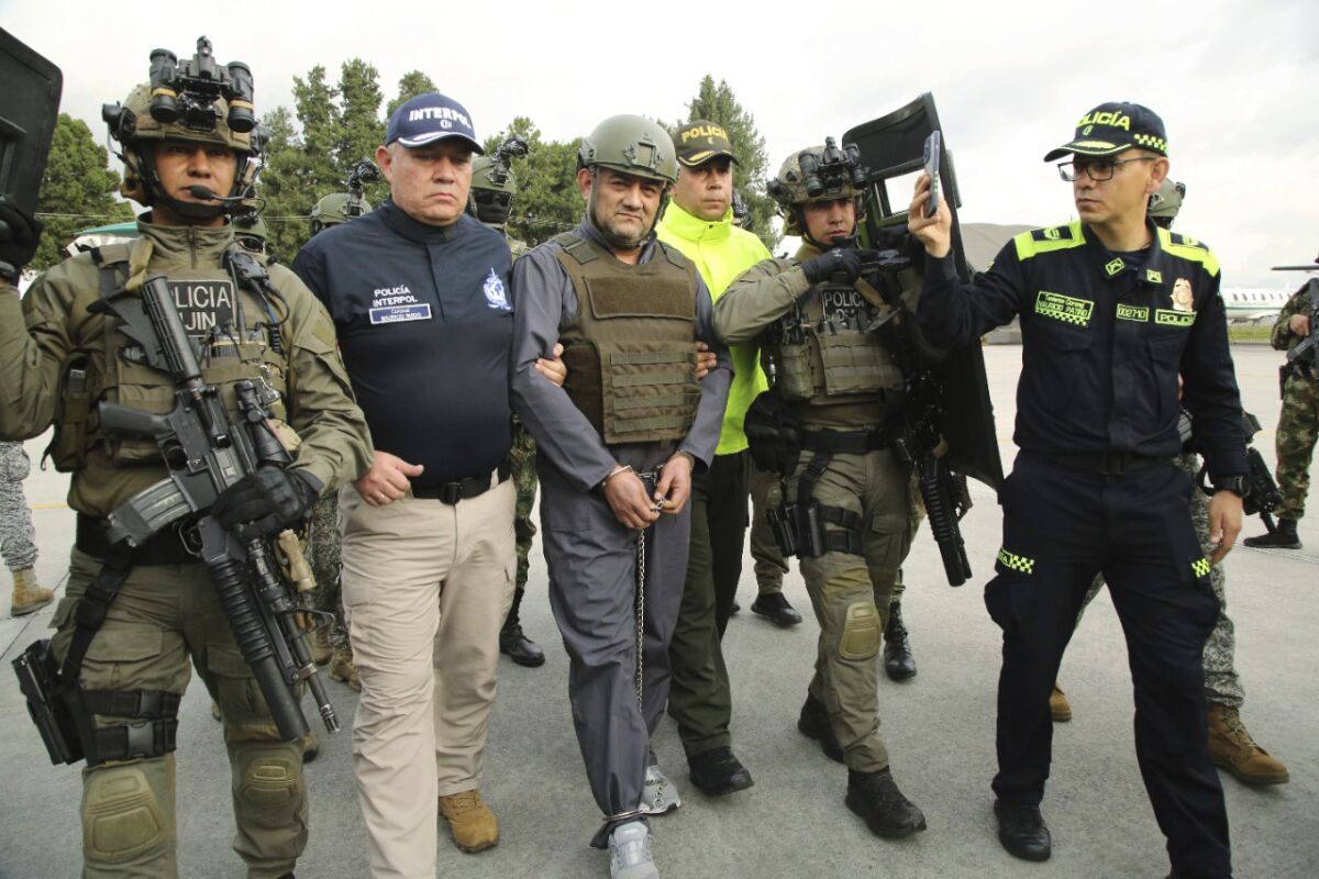 In this photo released by the Colombian Presidential Press Office, police escort Dairo Antonio Usuga, center, also known as "Otoniel," leader of the violent Clan del Golfo cartel prior to his extradition to the U.S., at a military airport in Bogota, Colombia, Wednesday, May 4, 2022. (Colombian presidential press office via AP)