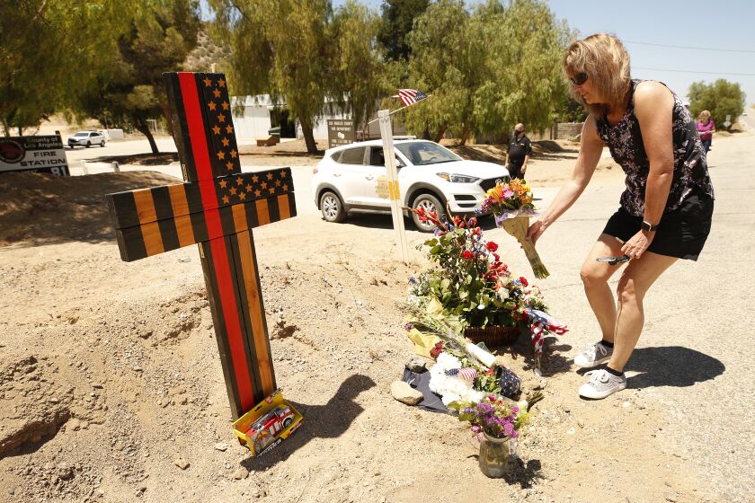 AGUA DULCE, CA - JUNE 04: Cindee Erdman, from the San Fernando Valley places flowers at a memorial featuring a cross made of wood along with flowers located outside Los Angeles County Fire Dept. Station 81 at 8710 Sierra Hwy in Agua Dulce where LA County Firefighter specialist Tory Carlon, 44, was killed in a shooting last Tuesday. The twenty-year veteran of the department was killed by fellow off-duty firefighter Jonathan Tatone, who opened fire wounding a Captain as well, then fled to his home in nearby Acton, barricaded himself inside, and set the house on fire before he was found dead. LA County Fire Station 81 on Friday, June 4, 2021 in Agua Dulce, CA. (Al Seib / Los Angeles Times).