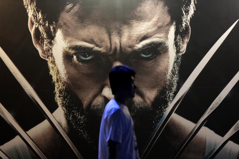 A man walks past a huge poster of a scowling superhero with long metal claws